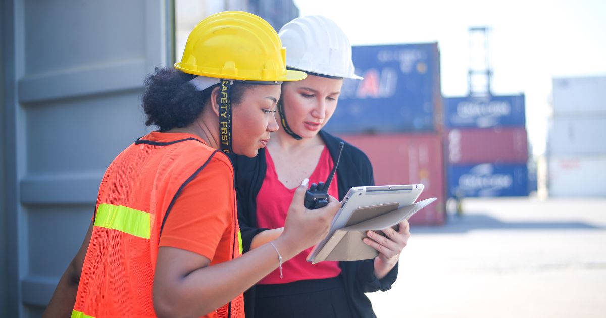 Dos mujeres con casco de seguridad industrial revisando una tablet en entorno energético, representando la digitalización del sector energético y la eficiencia operativa